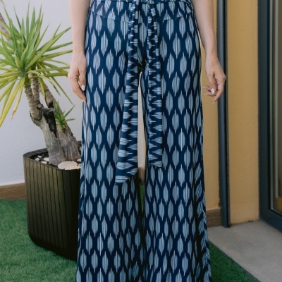 Calças largas com padrão azul e branco e cinto, usadas com blusa branca, em ambiente exterior com planta e relva artificial.