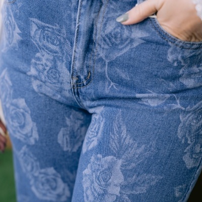 Calças de ganga azuis com padrão floral branco e mão feminina no bolso