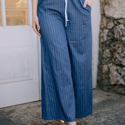 Calças largas azuis de riscas brancas com cordão branco na cintura e sandálias douradas em ambiente exterior