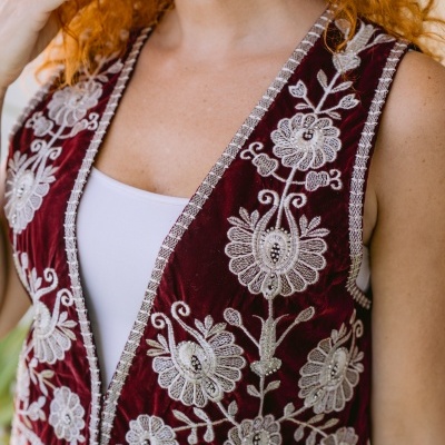 Colete de veludo vinho com bordado floral branco e prateado sobre camiseta branca.