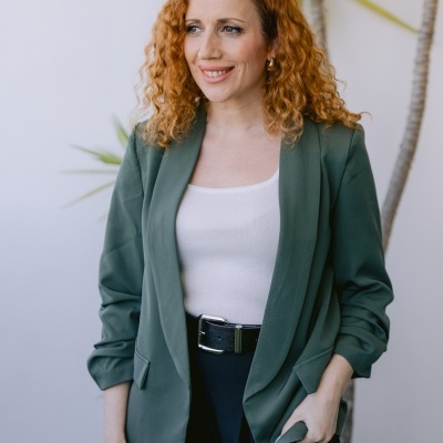 Mulher com blazer verde e top branco posando junto a uma planta