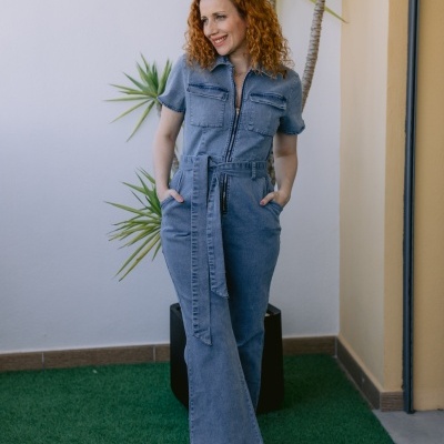 Mulher com macacão de ganga azul claro e ténis coloridos em ambiente exterior com plantas.