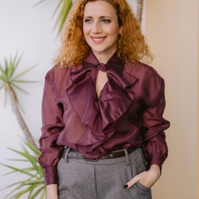 Mulher com blusa bordo folhos e calças cinzentas com renda