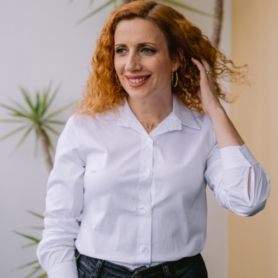 Mulher de camisa branca e calças pretas com plantas ao fundo