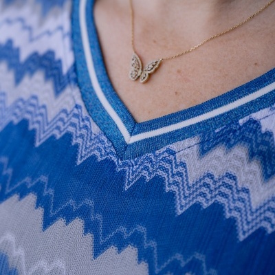 Colar com pendente de borboleta dourada num pescoço com camisola azul e branca com padrão zig zag