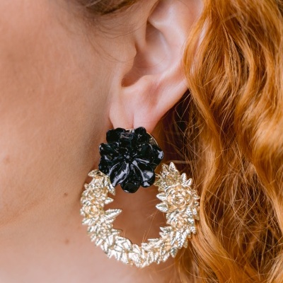 Brinco dourado floral com flor preta brilhante numa orelha