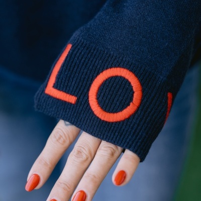 Manga de camisola azul escuro com letras laranja bordadas e mão com unhas laranja