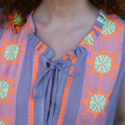 Blusa lilás com padrões laranja e verde e decote arredondado com laço