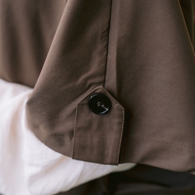 Detalhe de peça de vestuário marrom com botão preto e tecido branco