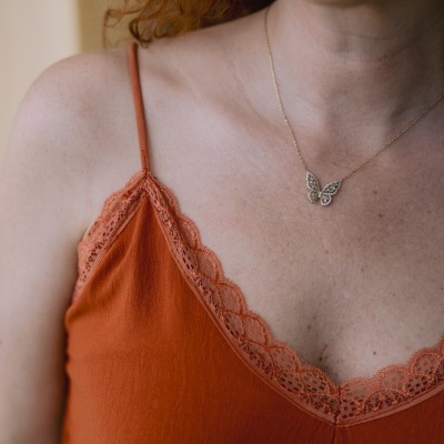 Blusa alaranjada com renda e colar de borboleta.