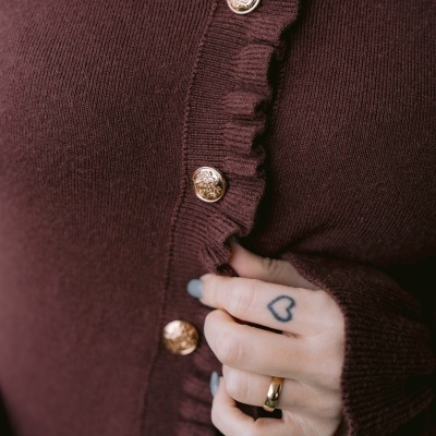 Cardigã castanho com botões dourados e punho com dedo tatuado e anel dourado