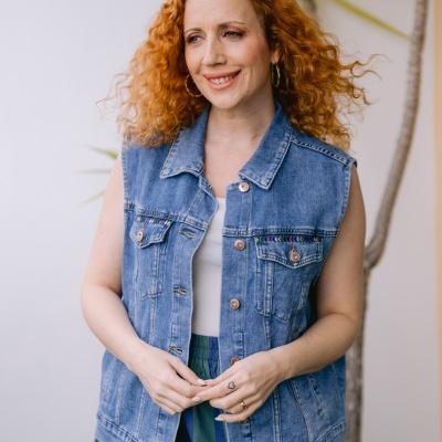 Colete jeans azul com detalhes bordados coloridos em fundo com planta e parede clara