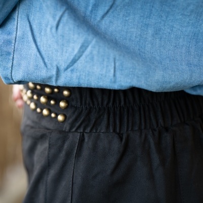 Calças pretas com tachas douradas na cintura e camisa azul