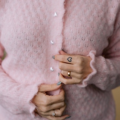Cardigan rosa com botões de coração e mãos com anéis