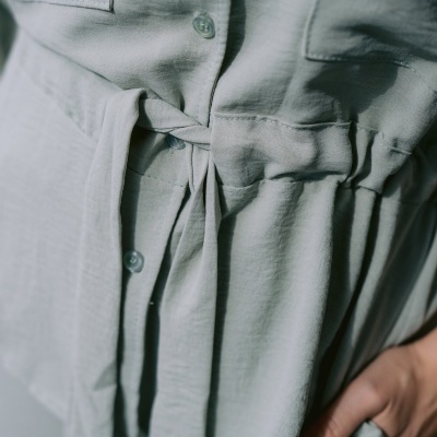 Peça de roupa cinzenta clara com botões e faixa para amarrar na cintura