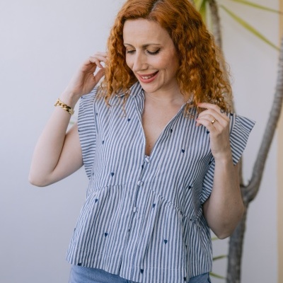 Blusa de mulher às riscas azul e branco com bordados azuis e botões, com jeans e planta ao fundo