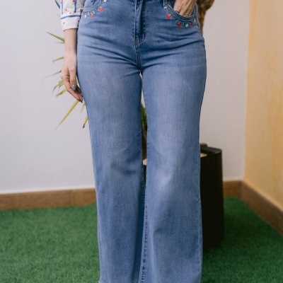 Calças de ganga azul claro com bordado floral colorido nas laterais dos bolsos frontais e camisa branca com padrão