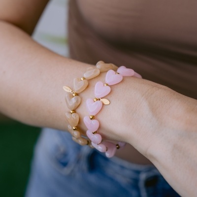 Pulseiras de coração em bege e rosa com detalhes dourados num pulso.