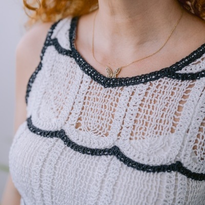 Blusa branca em tricô com ribetes pretos e colar dourado com borboleta