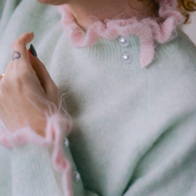 Camisola de malha com detalhes rosa e botões perolados vista em close-up no pescoço e braço