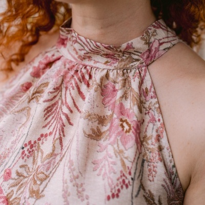 Blusa floral rosa com gola alta, usada por mulher ruiva e brincos dourados