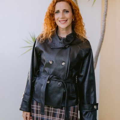 Mulher com casaco preto de pele e saia xadrez, com planta ao fundo