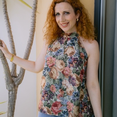 Mulher com blusa estampada floral e calças de ganga ao lado de planta em interior
