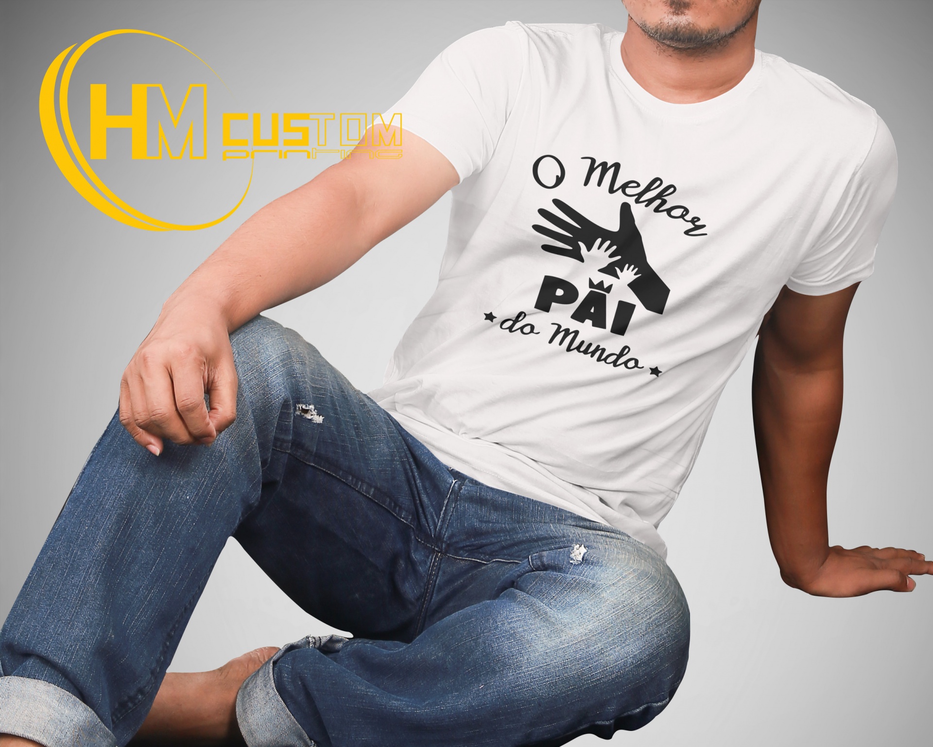 O Melhor Pai do Mundo Homem com t-shirt branca 'O Melhor PAI do Mundo' e calças de ganga azul sentado