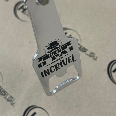 Porta-chaves metálico prateado com texto em preto e fundo bege com logótipos.