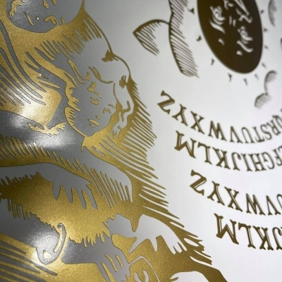 Tabuleiro Ouija branco com desenhos dourados e alfabeto em maiúsculas