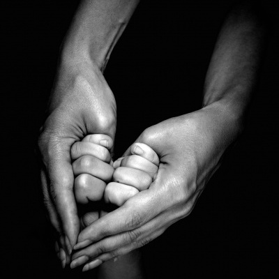 Mãos adultas segurando mãos de criança com fundo preto