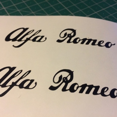 Folha branca com escrita 'Alfa Romeo' em preto sobre superfície verde com grelha branca