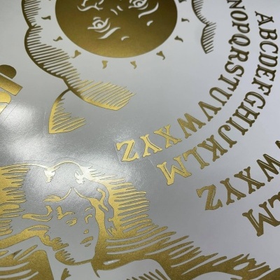 Tábua de Ouija com letras douradas e desenhos em fundo branco