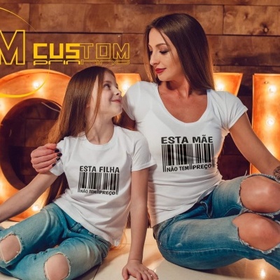 Mulher e criança sentadas com t-shirts brancas com textos e códigos de barras em ambiente rústico com letras luminosas