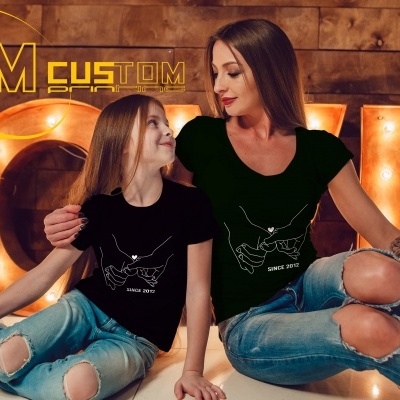 Duas pessoas com t-shirts pretas e jeans rasgados sentadas com luzes de letras atrás