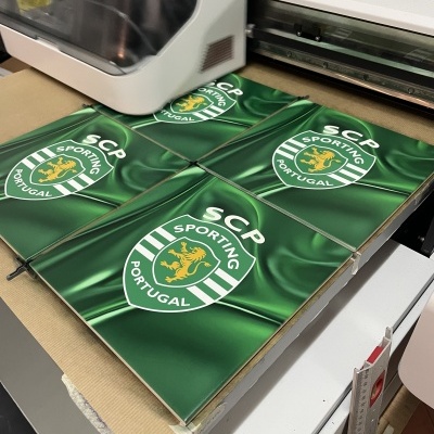 Quatro azulejos verdes com o emblema do SCP Sporting Portugal sobre mesa ao lado de impressora.