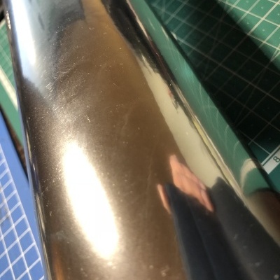 Rolo de filme metalizado prateado sobre superfície de corte verde com padrão de grade