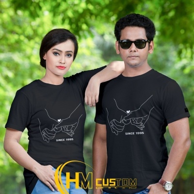 Dois modelos usam t-shirts pretas com estampa de mãos entrelaçadas e texto 'SINCE 1995' ao ar livre.