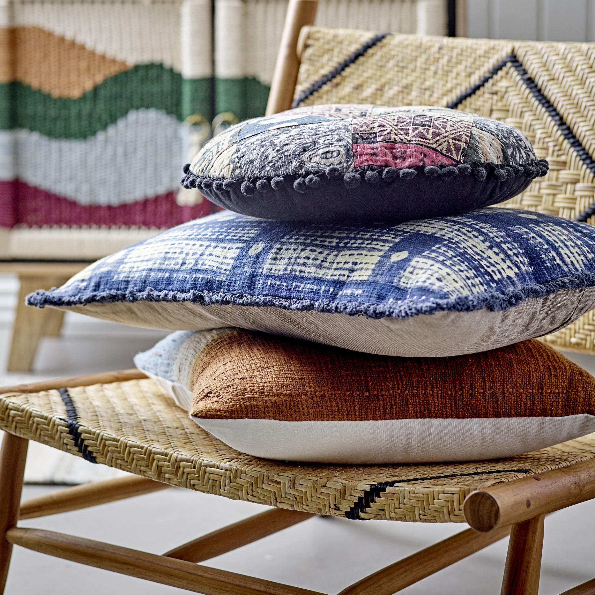 Cadeirão Lennox, madeira teca/rattan natural Três almofadas coloridas empilhadas em cadeira de madeira com assento em palha decorada