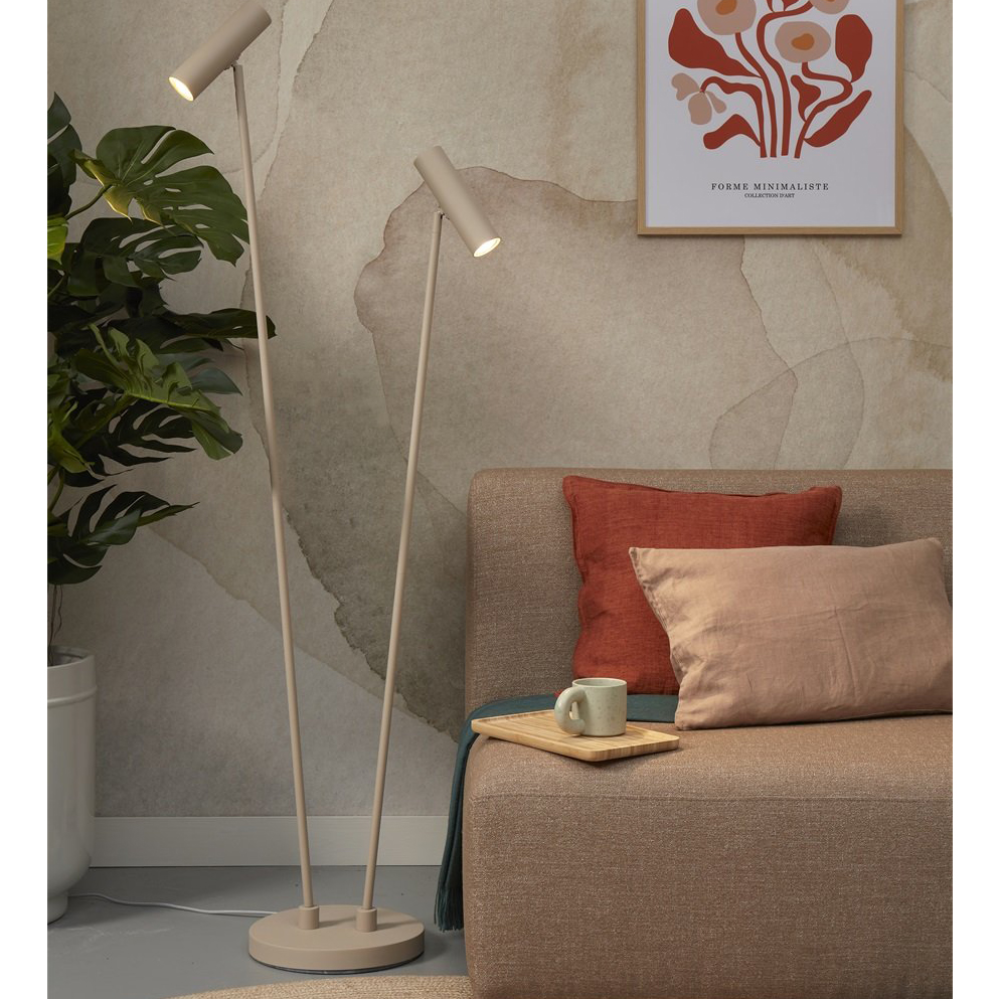 Candeeiro de Pé Havana com Duplo Foco Abajur de pé bege ao lado de sofá castanho com almofadas vermelho e bege, parede desgastada e quadro decorativo