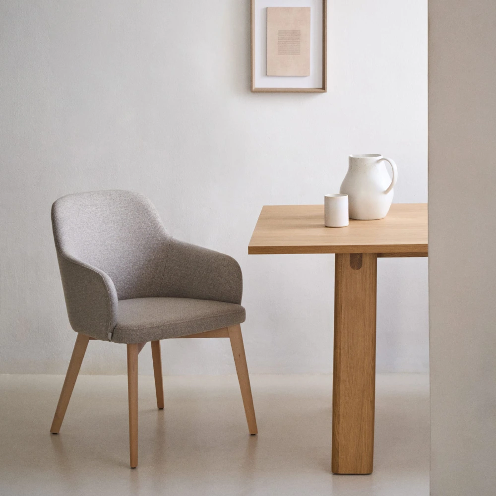 Cadeira estofada com braços em madeira faia Neli Cadeira cinza estofada e mesa de madeira clara com jarro e copo em parede branca