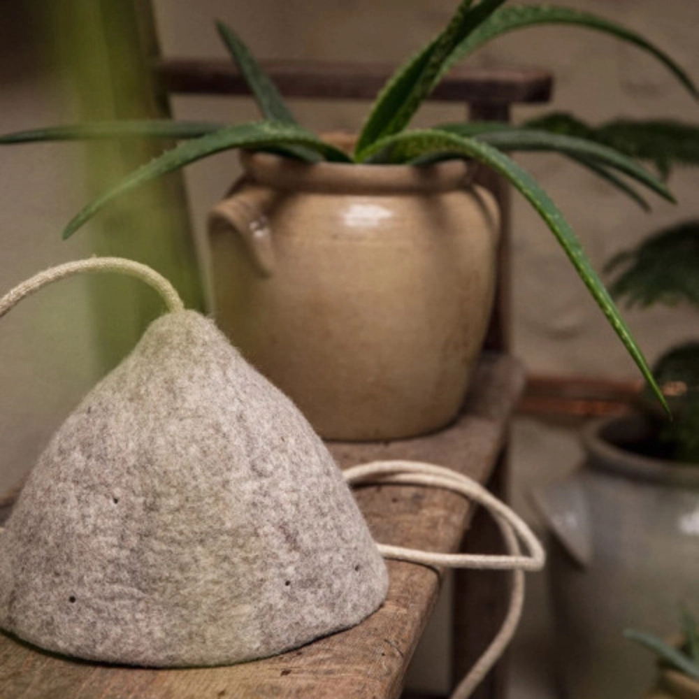 Candeeiro de Teto em Feltro Mármore Natural Tipi Ø22x16 Chapéu de feltro cinza claro sobre mesa de madeira com vasos cerâmicos e plantas ao fundo