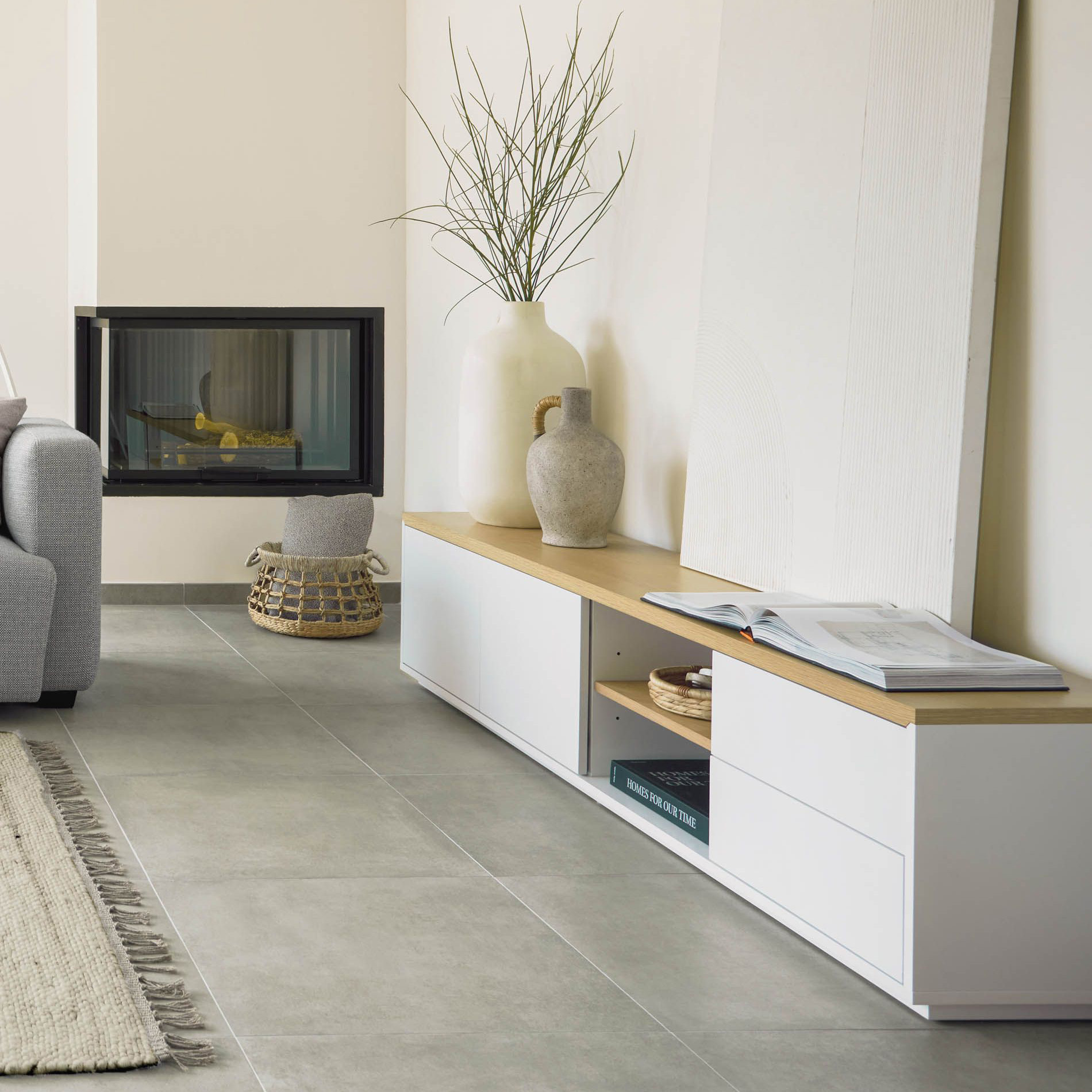 Móvel TV Abil, carvalho/lacado, 200x44 Móvel baixo branco com tampo de madeira clara, jarras cerâmicas decorativas, revista aberta e cesta de palha junto a lareira embutida.