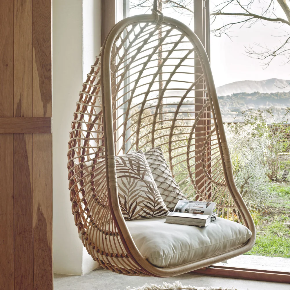 Cadeira suspensa Katerin, rattan natural Cadeira suspensa de rattan com almofadas ao lado de janela grande
