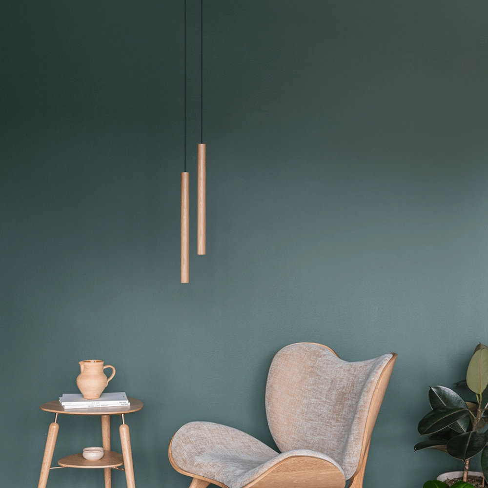 Candeeiro de Teto Chimes Tall em Madeira de Carvalho – 44 cm Interior moderno com cadeira reclinável cinza, mesa lateral com jarro, luminárias pendentes de madeira e parede verde-escura.