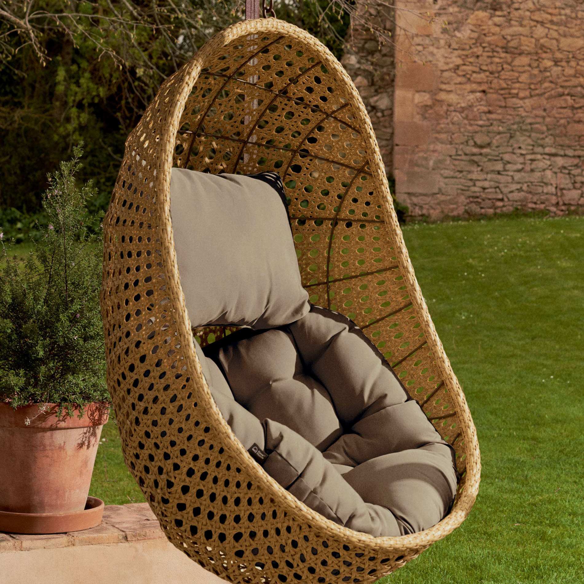 Cadeira suspensa Siran, rattan sintético, bege Cadeira suspensa de vime com almofadas cinzentas num jardim