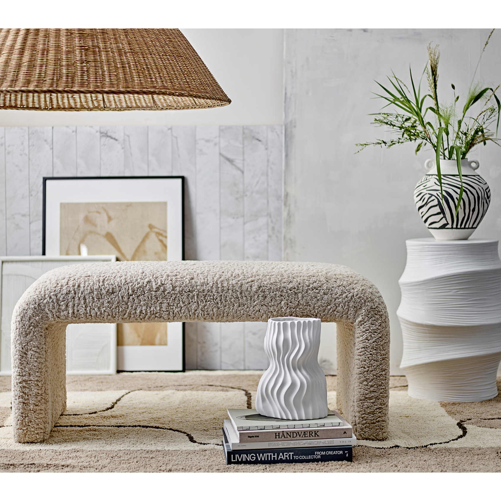 Banco Bobbie, madeira, bouclé, natureza, 100x45 Banco estofado branco felpudo sobre tapete bege com linhas pretas, vasos decorativos e quadro na parede cinza clara.