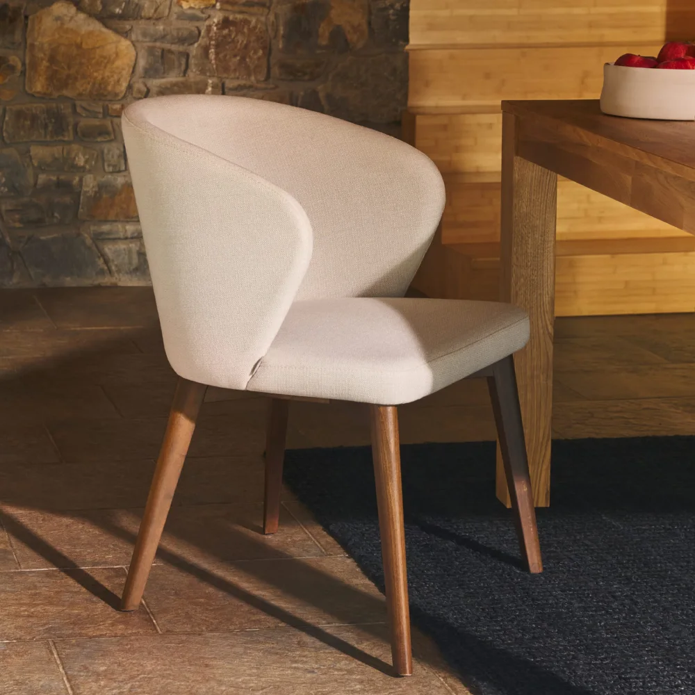 Cadeira estofada com braços em madeira faia Darin Cadeira estofada bege com pernas de madeira junto a mesa num interior rústico