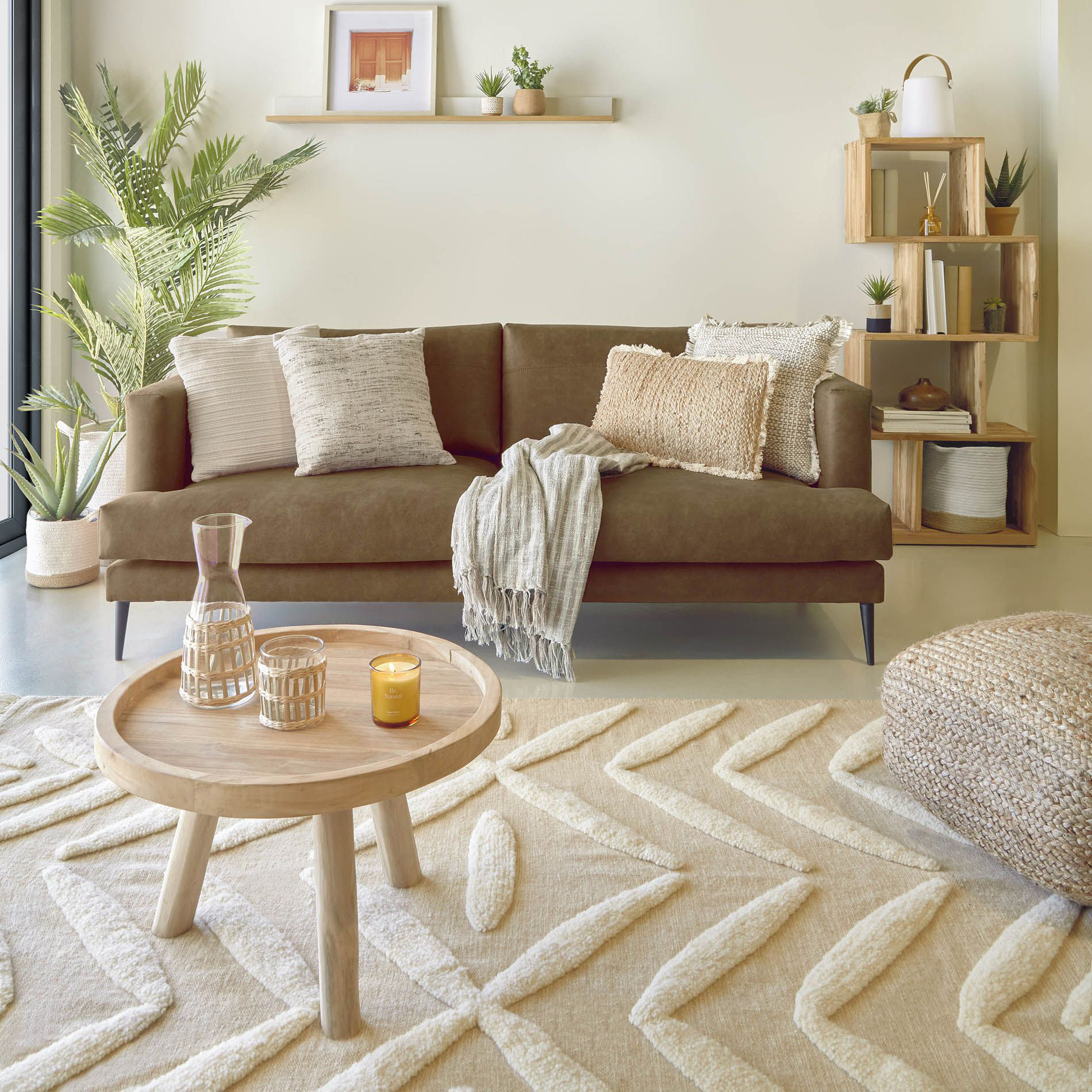 Mesa de centro Genda, madeira teca, Ø55x36 Sala com sofá castanho, almofadas, mesa redonda, tapete creme com padrão geométrico e estante com plantas.