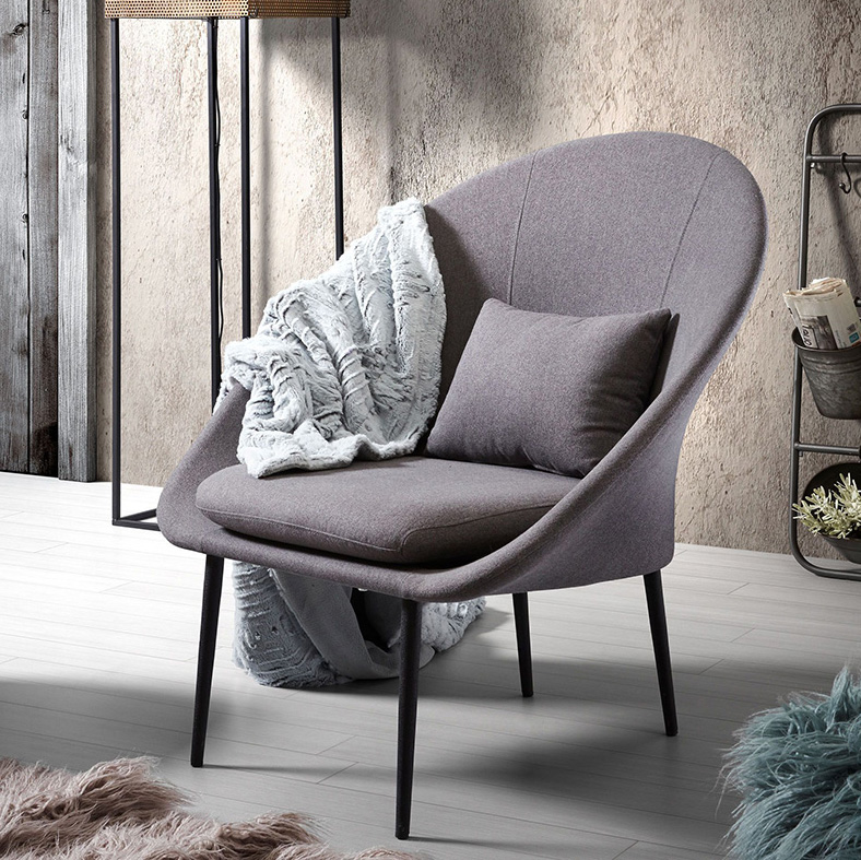 Poltrona Northdam, estofado, cinza Cadeira cinzenta com almofada e manta junto a candeeiro e prateleira num ambiente interior